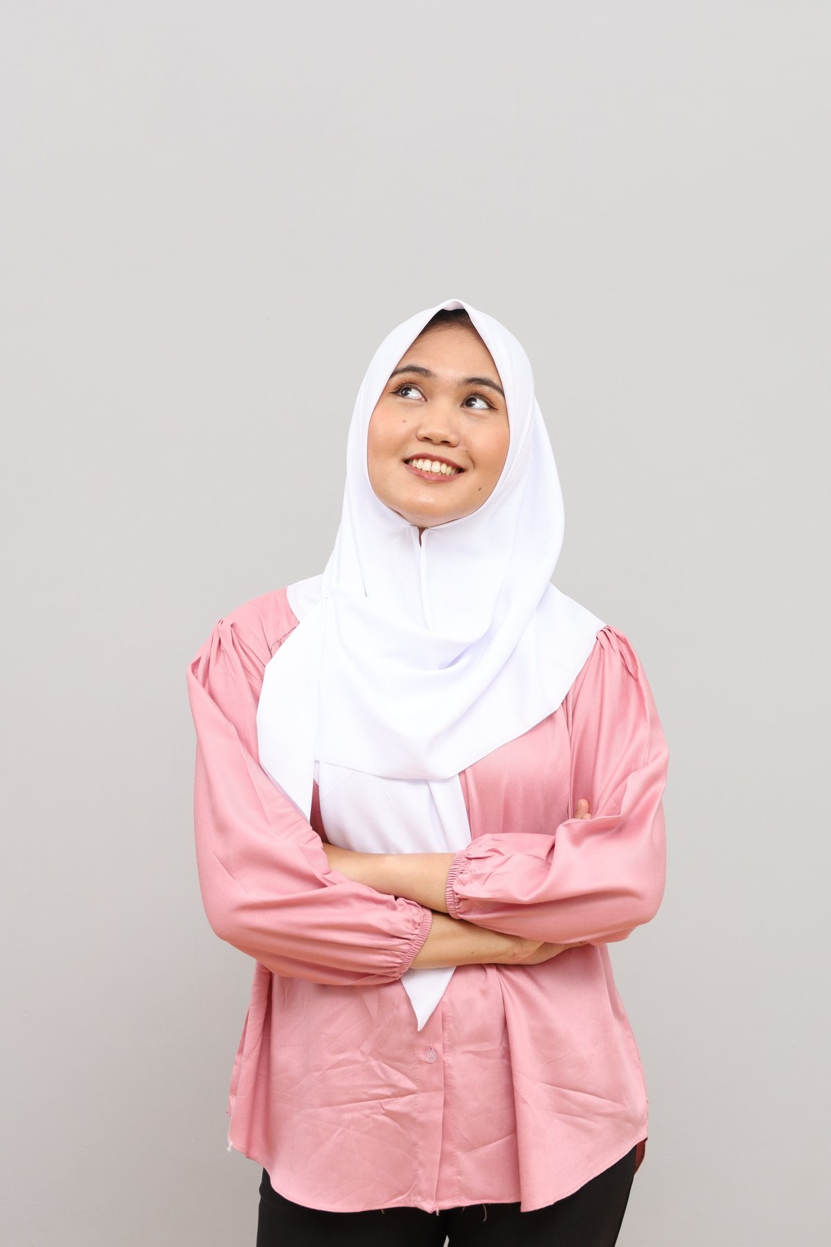 A woman in hijab, smiling peacefully with hands folded